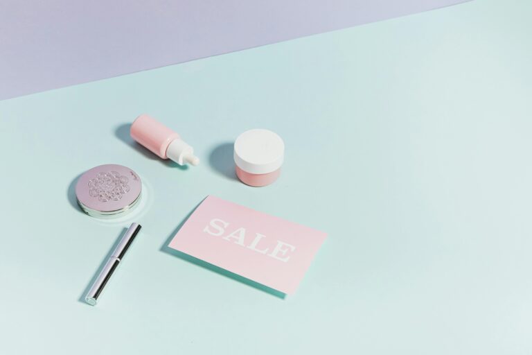 Clean flat lay of pastel pink beauty products and sale card on a light background.